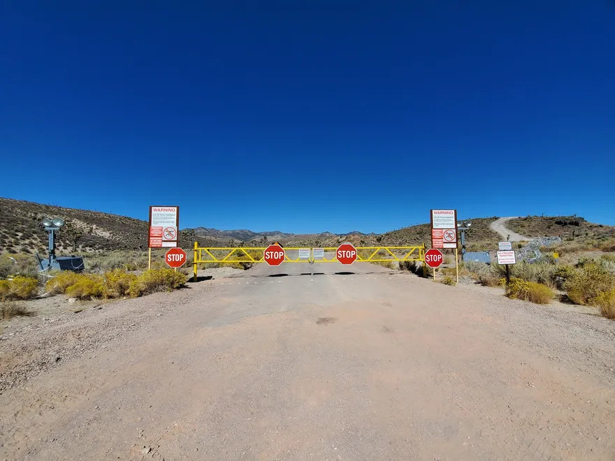 Portón principal de acceso a Area 51, con cerco perimetral y cartel de advertencia junto a la ruta de tierra.